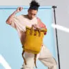 Man Holding Folding Top Mustard Backpack with Clip Closure