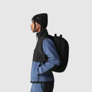 side view of person in black and blue jumper carrying a black branded bag on their bag