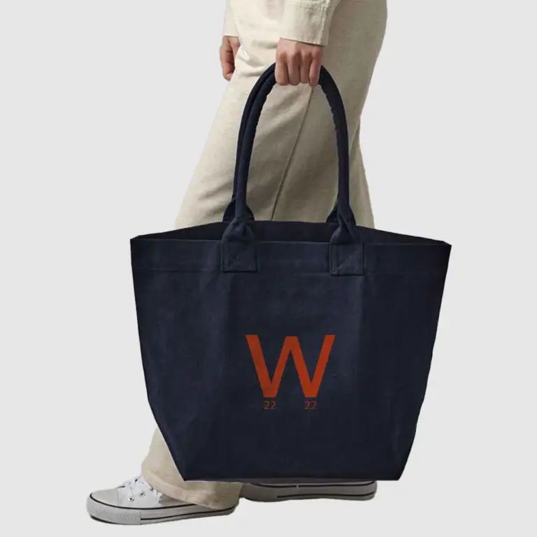 person in cream clothing carrying a navy blue canvas bag with orange print