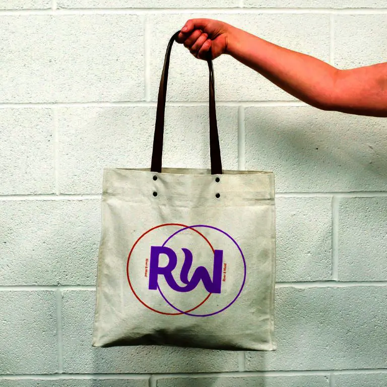 hand holding natural bag with leather handles and metal rivets. Print is orange and pink