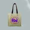 front view of a natural bag with leather handles and metal rivets. Print is orange and pink