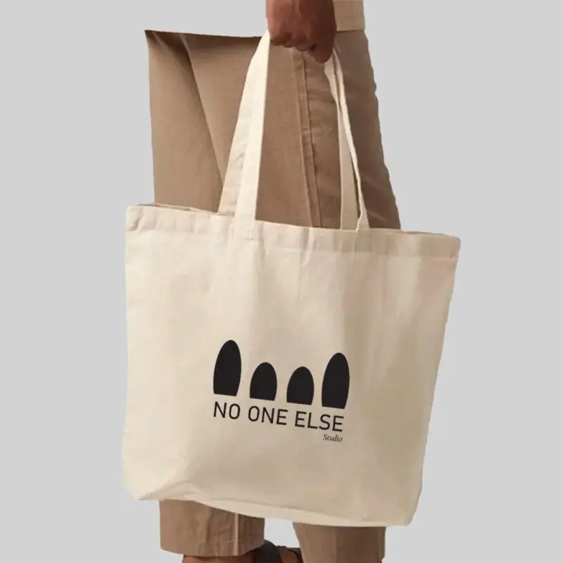 person wearing brown trousers holding a natural coloured bag with black print