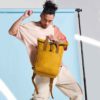 Man Holding Folding Top Mustard Backpack with Clip Closure