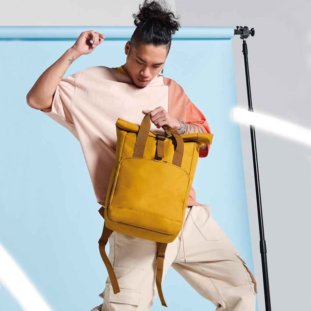 Man Holding Folding Top Mustard Backpack with Clip Closure