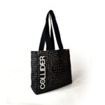 side view of black square tote bag with black handles hanging off hook. The bag is black with white check print and white text that spells COLLIDER