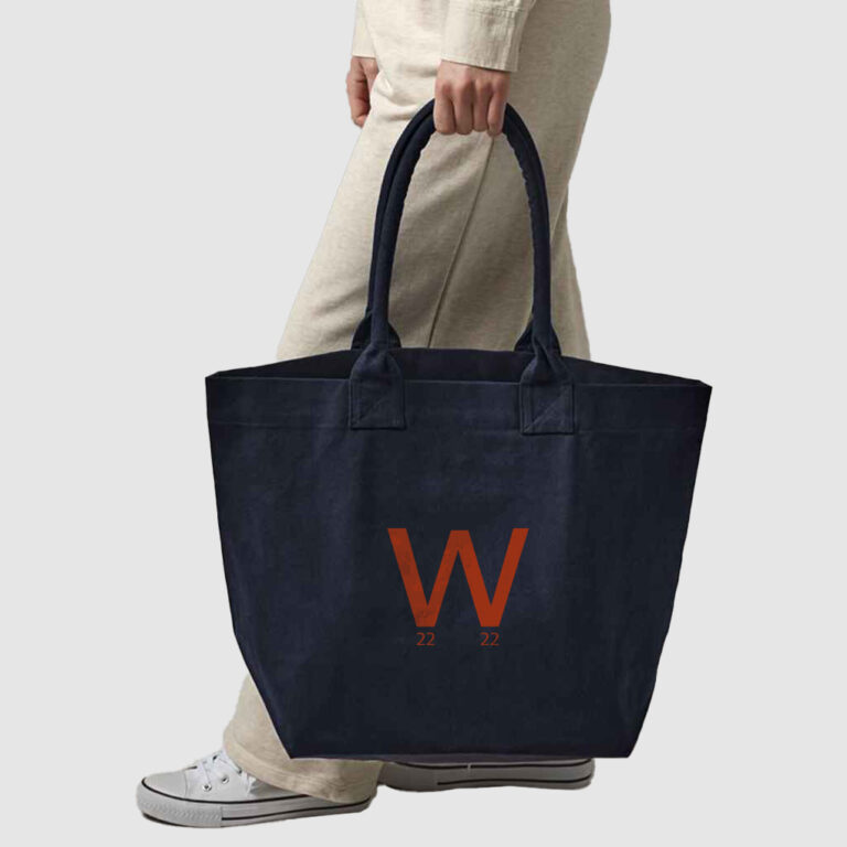 person in cream clothing carrying a navy blue canvas bag with orange print