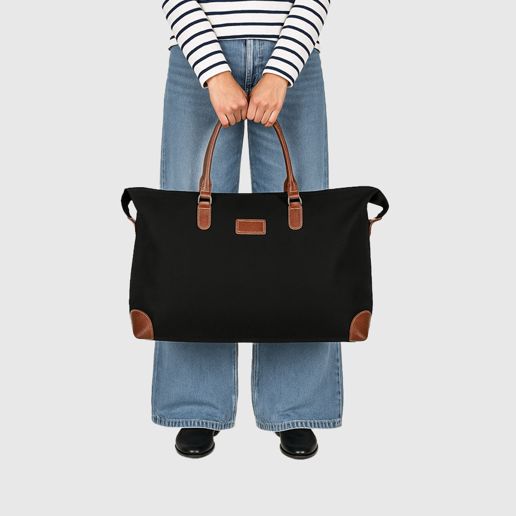 person in blue jeans and stripey top holding black luggage bag in front of them