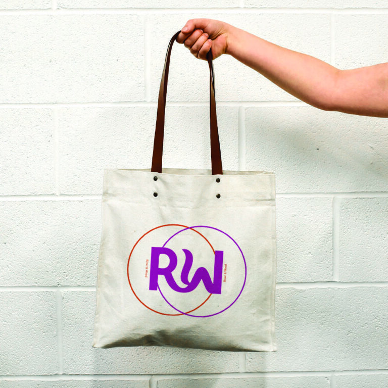 hand holding natural bag with leather handles and metal rivets. Print is orange and pink