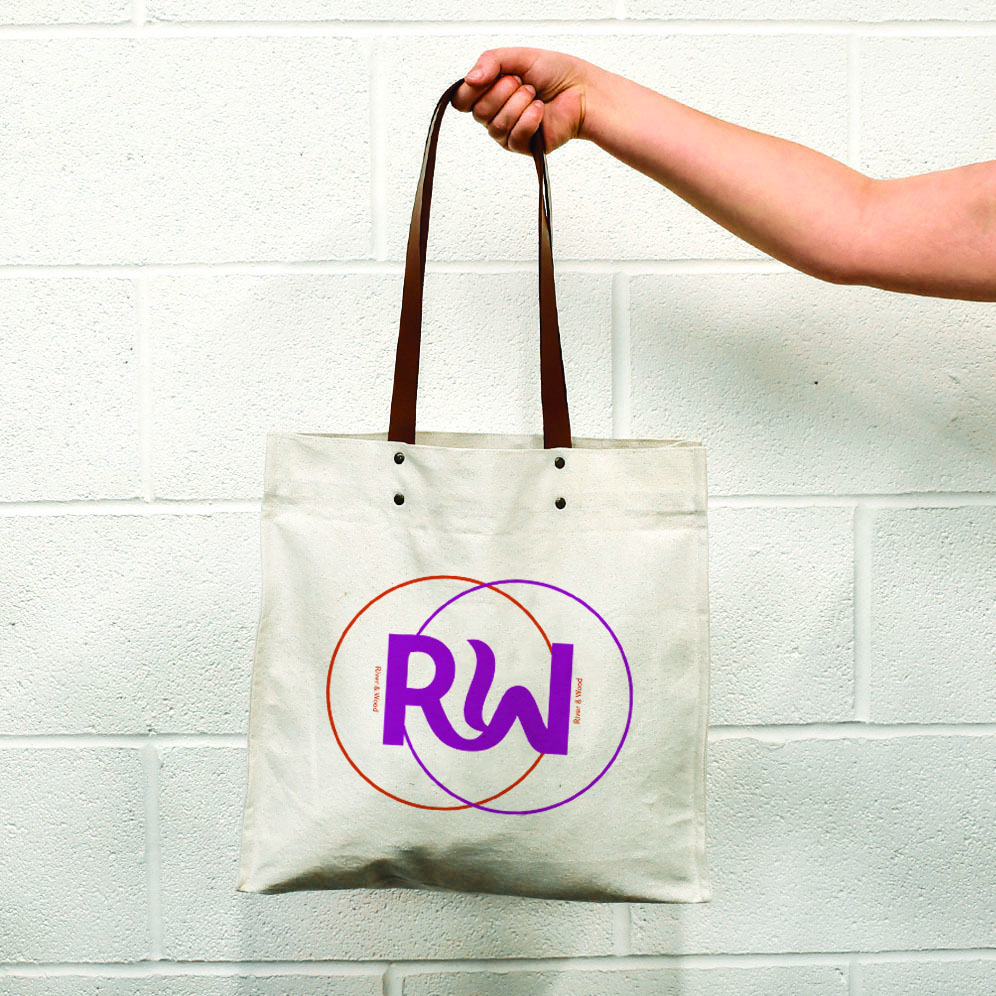 hand holding natural bag with leather handles and metal rivets. Print is orange and pink