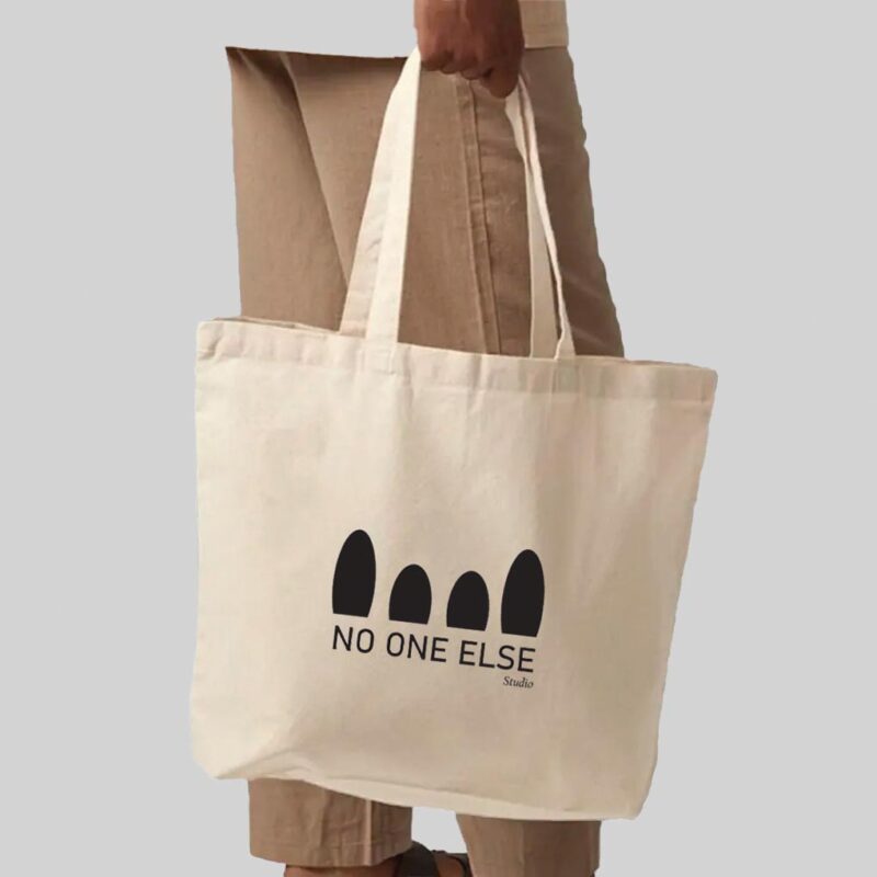 person wearing brown trousers holding a natural coloured bag with black print