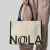 hand holding natural bag with black handles and black print