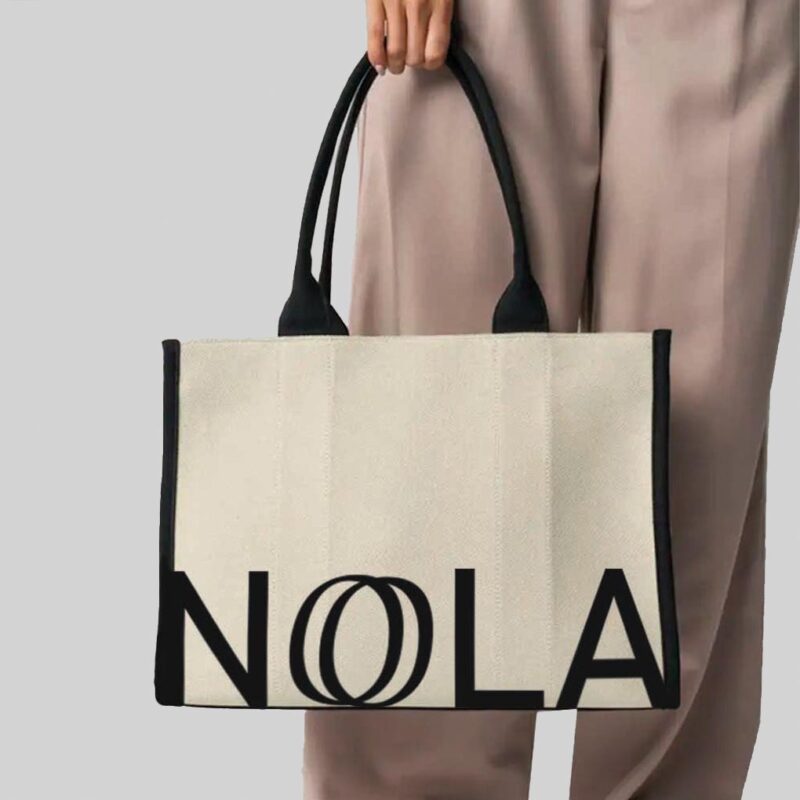 hand holding natural bag with black handles and black print