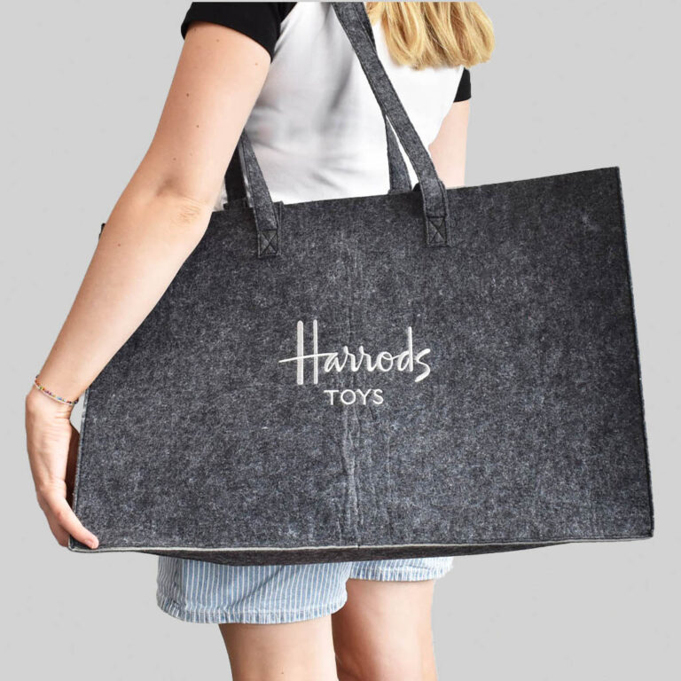 person carrying Harrods tote bag in grey felt