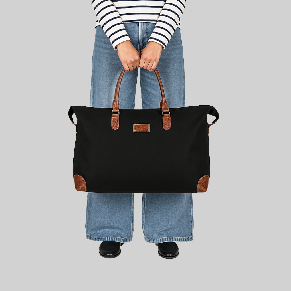 person in striped top and blue jeans holding black overnight bag with tan leather handles