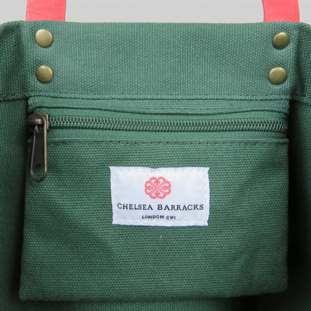 Green canvas tote bag with pink PU leather detail and woven label on inside pocket