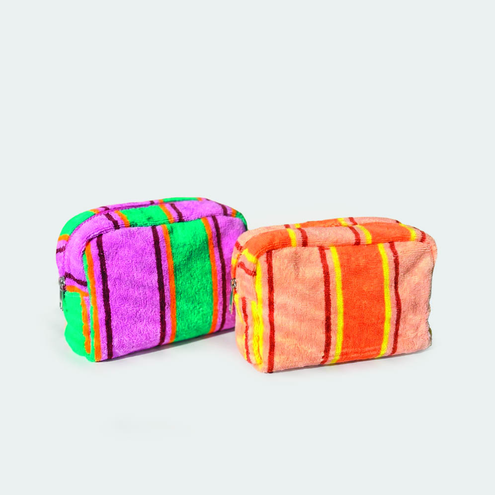 two colourways of terry cloth wash bags next to one another. They are closed and one is green and pink striped one is orange and peach striped